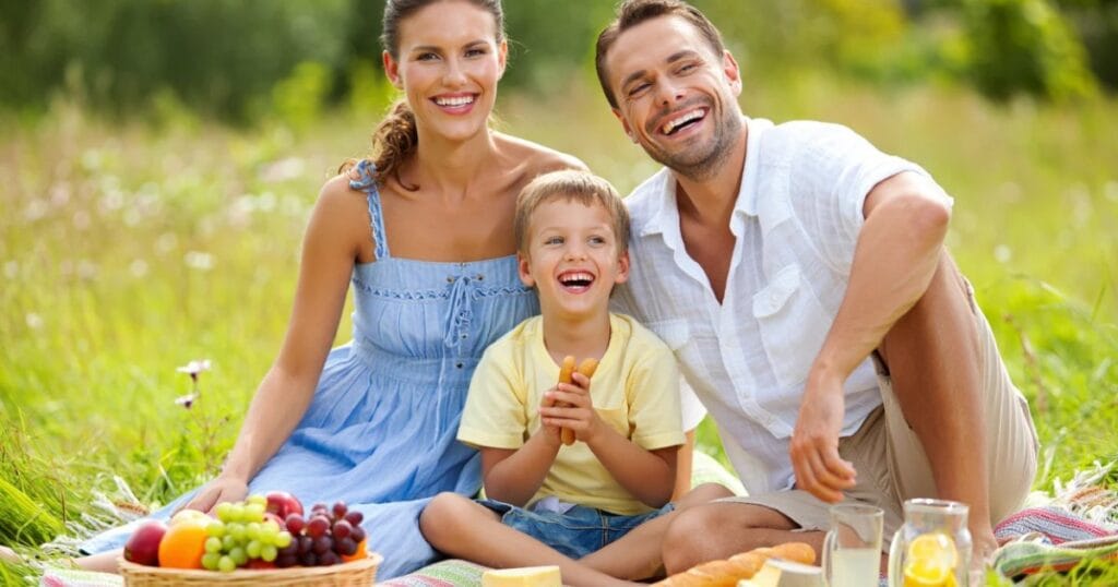Familia sonriente disfrutando un picnic al aire libre, protegida con un plan del Mercado de Salud